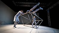 Fotografi på tre personer som gör akrobatik på kub i stål.
