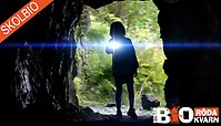 Fotografi på ett barn som står och lyser med ficklampa i en grottöppning.